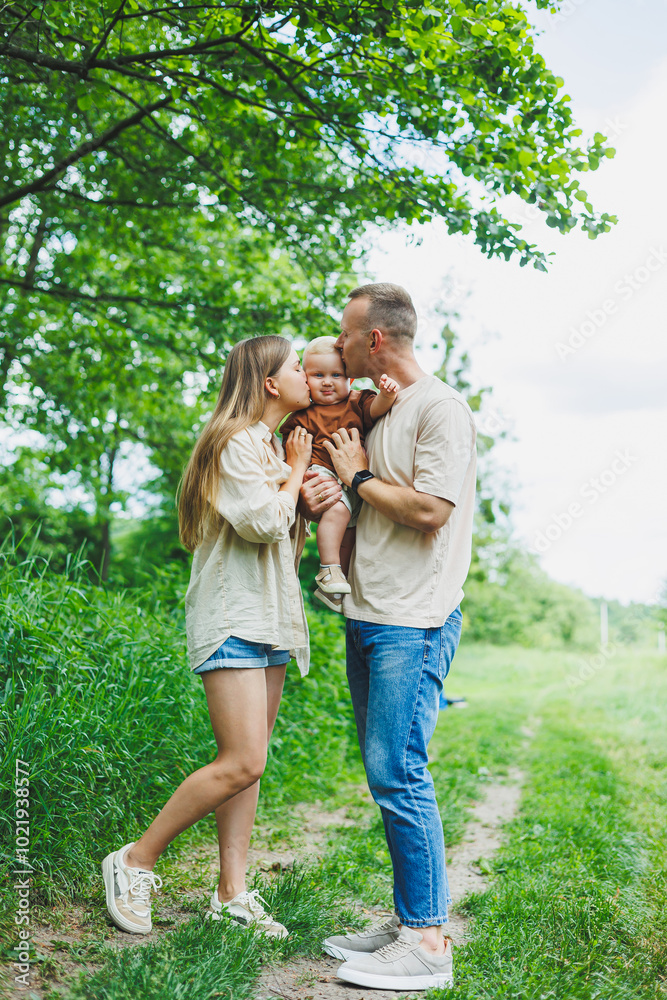 Fototapeta premium A family couple with a small son are standing in the park on the grass. Mother, father and child walk. Happy family with a child.
