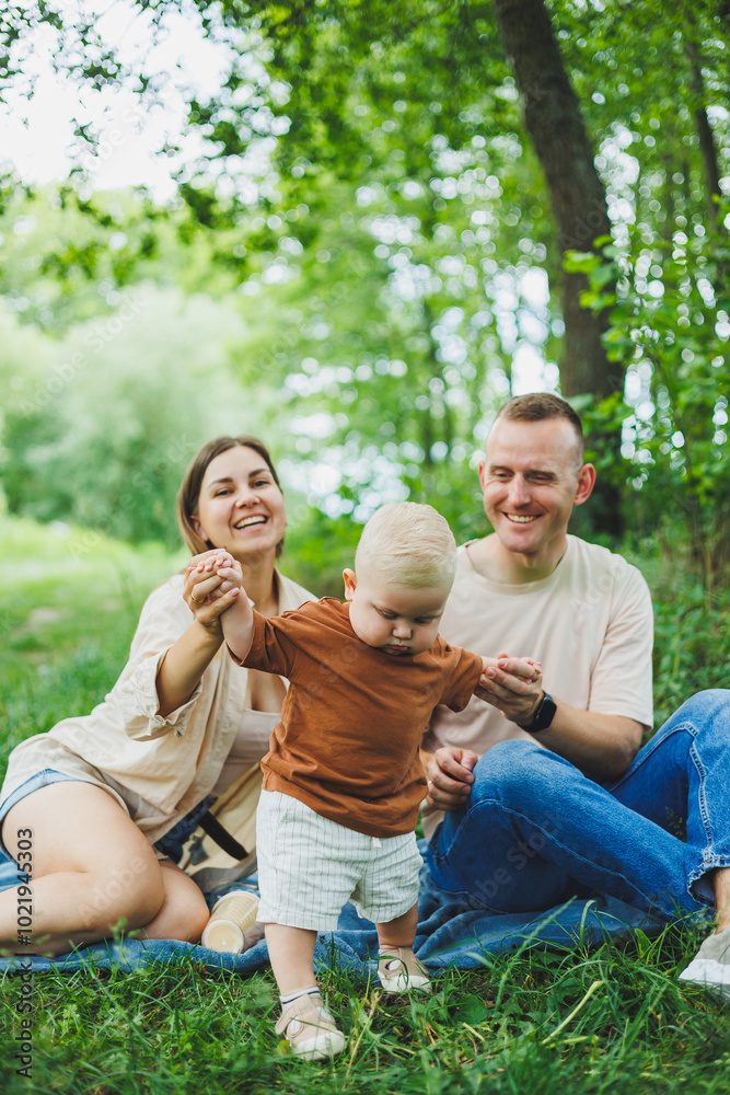 A family of a mother and father with a child in their arms, sitting in the park in the summer. The concept of a happy family with a small child, care and love. Happy family with a child. A family of a mother and father with a child in their arms, sitting in the park in the summer. The concept of a happy family with a small child, care and love. Happy family with a child.