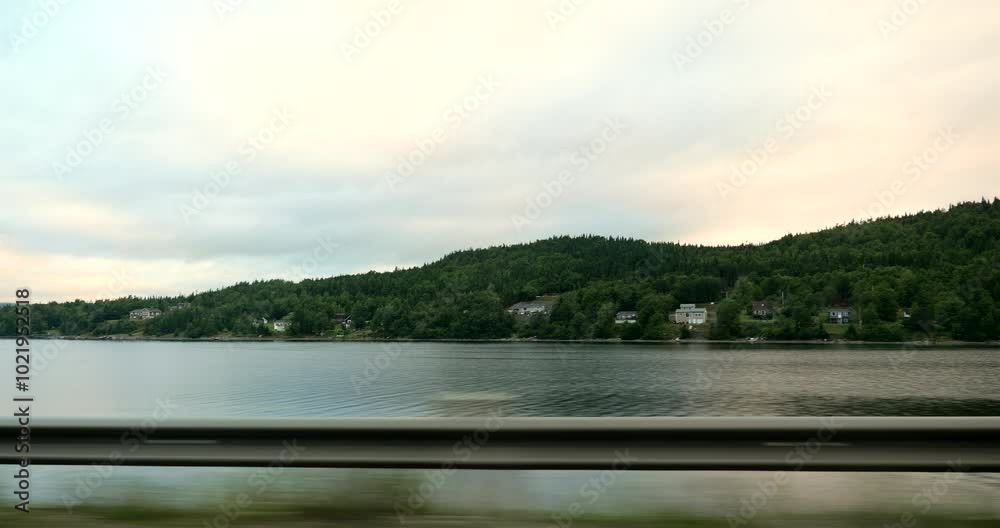 Side driving plate on a highway through a forested area and lake in Ontario, Canada. Road surrounded by dense trees under partly cloudy sky. Forest travel and nature exploration concept