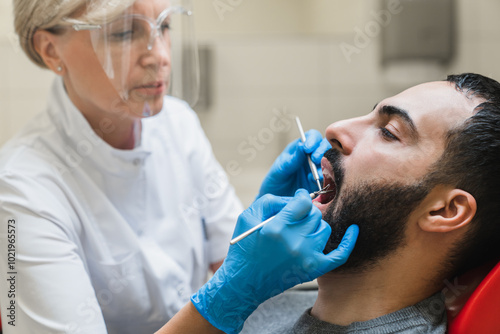 Stomatological checkup concept. Male Middle-Eastern patient visiting female dentist orthodontist. Dental equipment mirror. Teeth whitening.