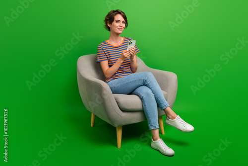 Full length photo of cute positive person sit comfy chair use smart phone isolated on green color background