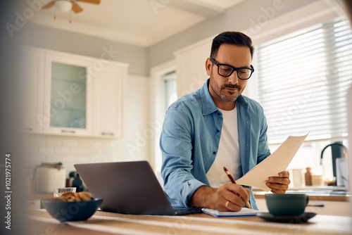 Foto Mid adult man taking notes while going through home finances.