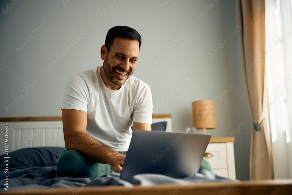 Happy man surfing net on laptop while enjoying in bed in morning. Happy man surfing net on laptop while enjoying in bed in morning.