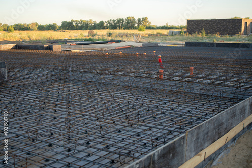 A steel-reinforced Swedish plate foundation is being constructed, with organized rebar laid out on the subgrade, ready for concrete pouring in a natural setting photo