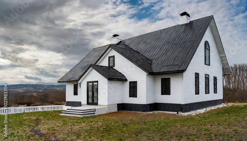 Modern white house with black accents nestled in a serene landscape surrounded by nature under a cloudy sky