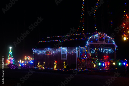 A small cottage festively decorated with Christmas lights and themed figures stands under tall light strings in a city park in northeast Ohio.