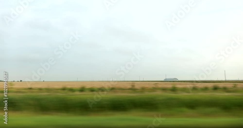 Driving plate side view on a highway through open plains and farmland in Midwestern United States agricultural fields under a wide sky rural travel and American heartland concept