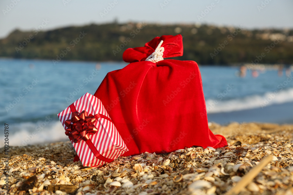 Red Santa bag and gift box on sea beach. Christmas vacation concept Red Santa bag and gift box on sea beach. Christmas vacation concept