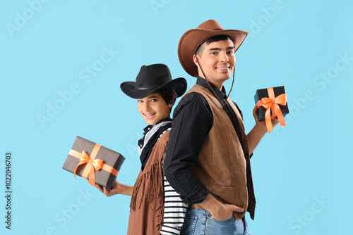 Little boy and his father dressed for Halloween as cowboys with gifts on blue background photo