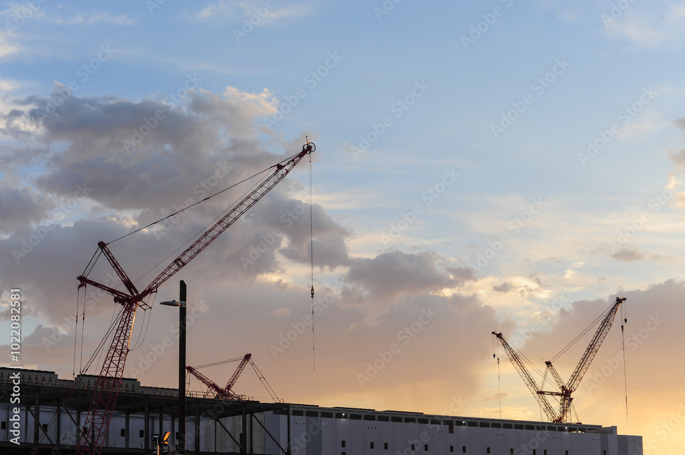 Sunset light bathes tower cranes rising over a building under construction in the southeastern corner of Maricopa County, Arizona Sunset light bathes tower cranes rising over a building under construction in the southeastern corner of Maricopa County, Arizona