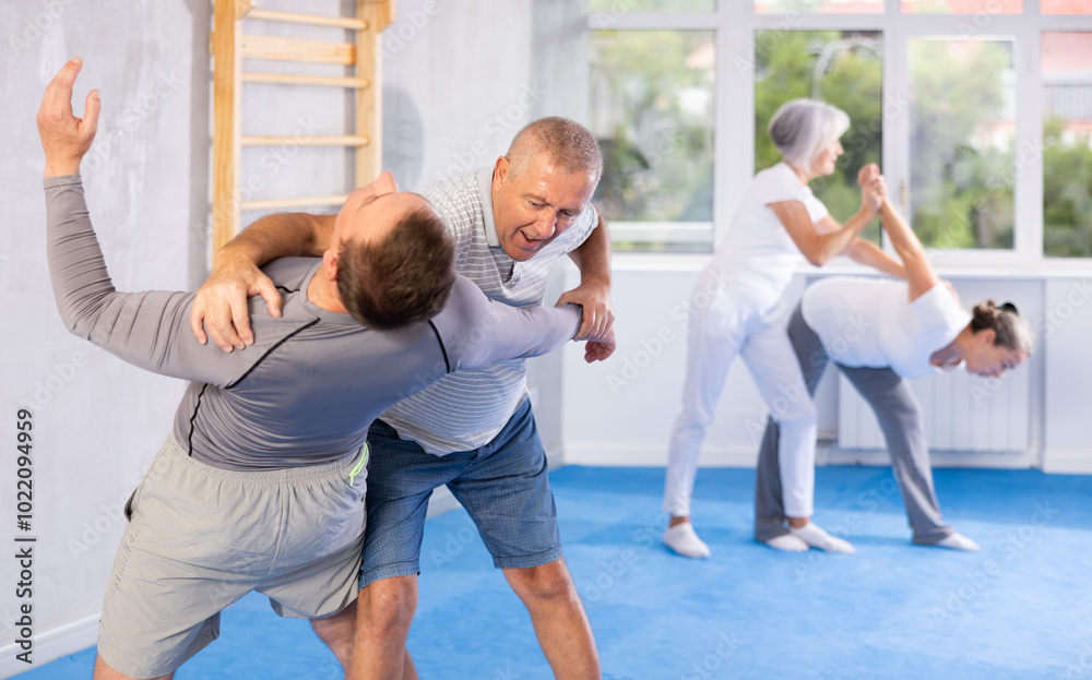 Obraz premium Mature man at a self-defense lesson learns how to make painful blows with his hand and foot