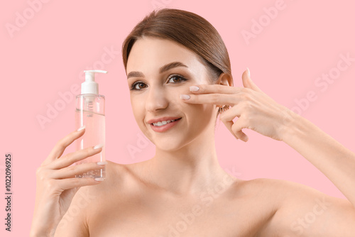 Beautiful young woman with bottle of cosmetic product on pink background