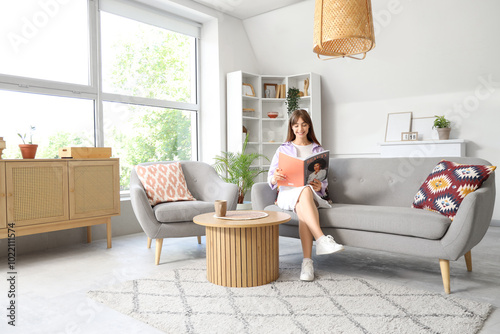 Young woman reading magazine on sofa at home