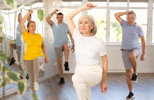 Expressive cheerful woman participating in upbeat Zumba class for group of seniors in mirrored fitness studio.. photo