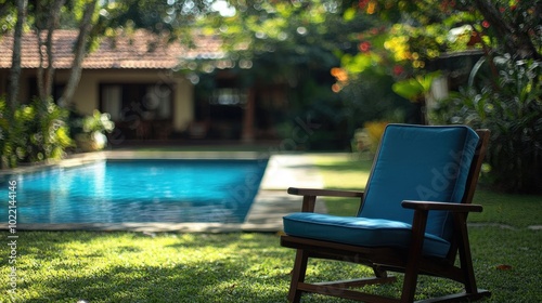 Relaxing blue chair by pool. A blue lounge chair with a wooden frame sits by a pool in a tropical garden, inviting you to unwind and enjoy the serene surroundings.