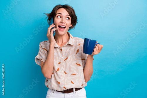 Photo of pretty cheerful lady hold cacao mug speak chatting telephone isolated on blue color background