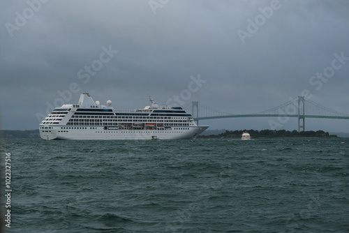 Small luxury cruiseship cruise ship liner Nautica anchoring at sea in bay of Newport, Rhode Island on grey cloudy day with swell, bridge and tender boats