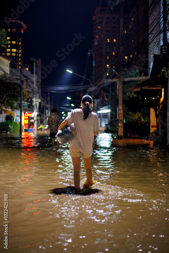 flood victims woman stands in the flooded streets of Chiang Mai city at night 2024, holding a bag with personal belongings. Another person wades ahead through the water