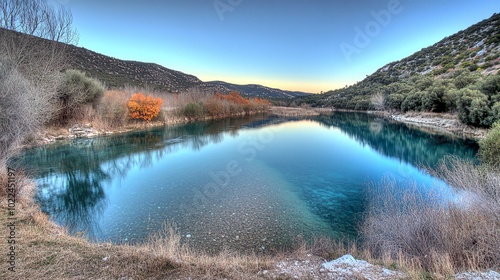 A serene lake nestled between hills, with crystal clear waters reflecting the surrounding autumn foliage.