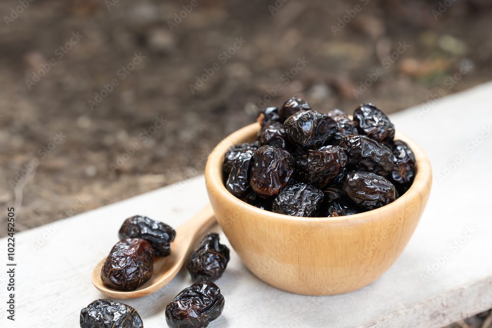 Close-up of a wooden bowl filled with dried date palm, accompanied by a wooden spoon holding a few dried date palm on a rustic white surface.