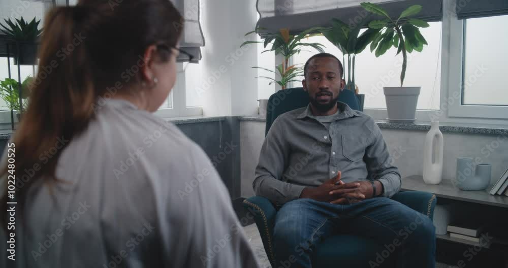 African American adult man sits in chair, talks to female psychologist, discuses problems on counseling session. Back view of therapist listening patient, providing therapy. Psychology, mental health. African American adult man sits in chair, talks to female psychologist, discuses problems on counseling session. Back view of therapist listening patient, providing therapy. Psychology, mental health.