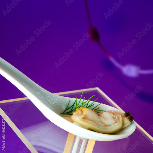 Clam in porcelain spoon on purple background