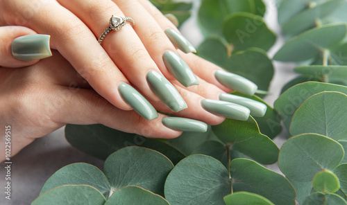 Elegant hands with green nails resting among lush eucalyptus leaves in a serene setting