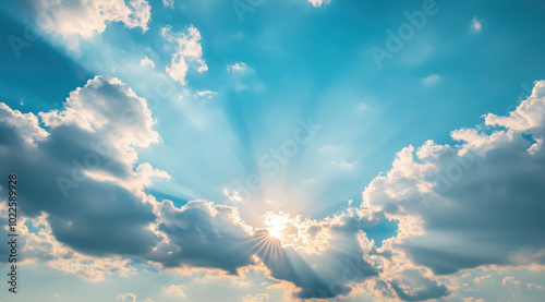 Sunlight streams through a cluster of white clouds on a clear day, casting soft rays across the azure sky, creating a serene and uplifting atmosphere.