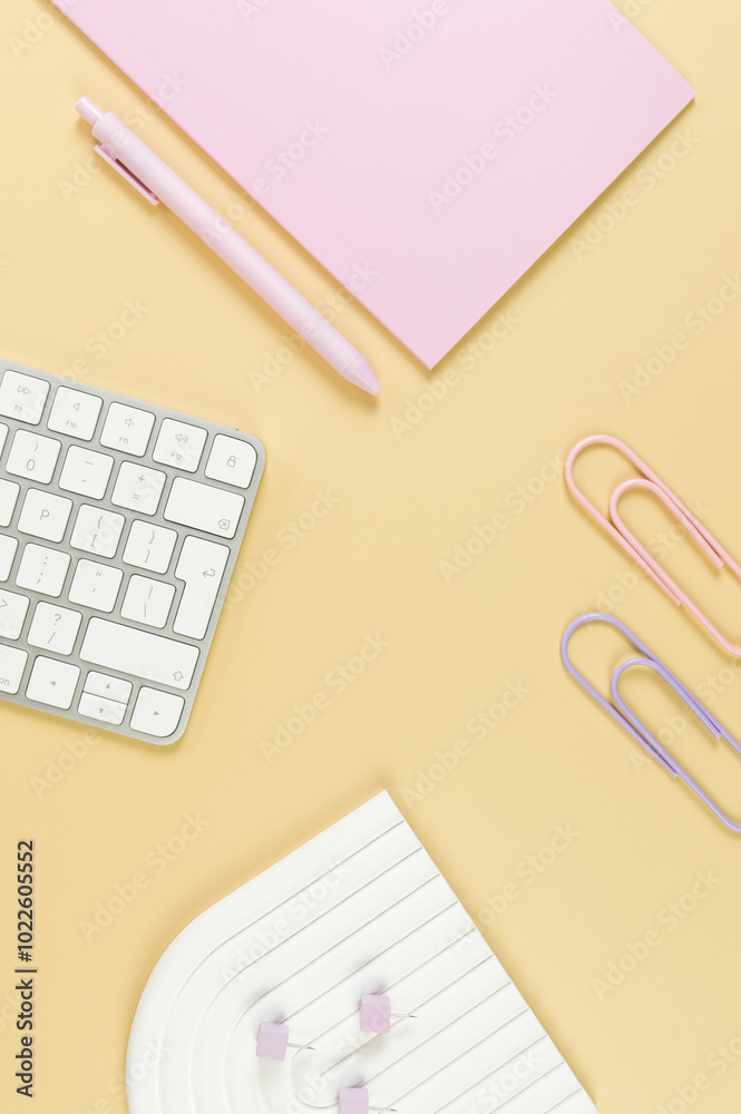 Top view of white keyboard, pink notebook, pink pen on yellow background. Paper clips, pins, modern office, school. White arch tray, flat lay, copy space. Top view of white keyboard, pink notebook, pink pen on yellow background. Paper clips, pins, modern office, school. White arch tray, flat lay, copy space.