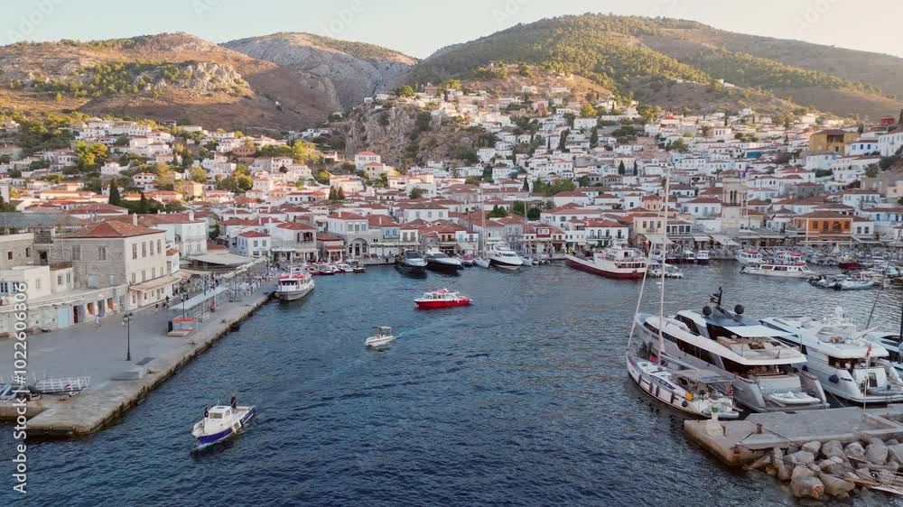 Explore the stunning aerial views of Hydra, Greece as the sun sets over the harbor, illuminating the vibrant boats and the cozy white buildings that grace the island. Explore the stunning aerial views of Hydra, Greece as the sun sets over the harbor, illuminating the vibrant boats and the cozy white buildings that grace the island.