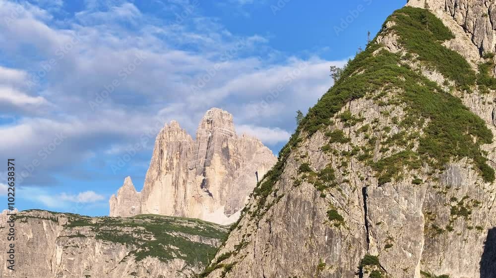 The towering peaks of the Dolomites rise against a backdrop of bright blue sky and scattered clouds The towering peaks of the Dolomites rise against a backdrop of bright blue sky and scattered clouds