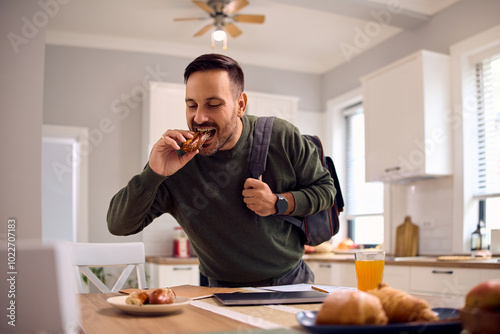 Man in  rush eating sandwich in kitchen.