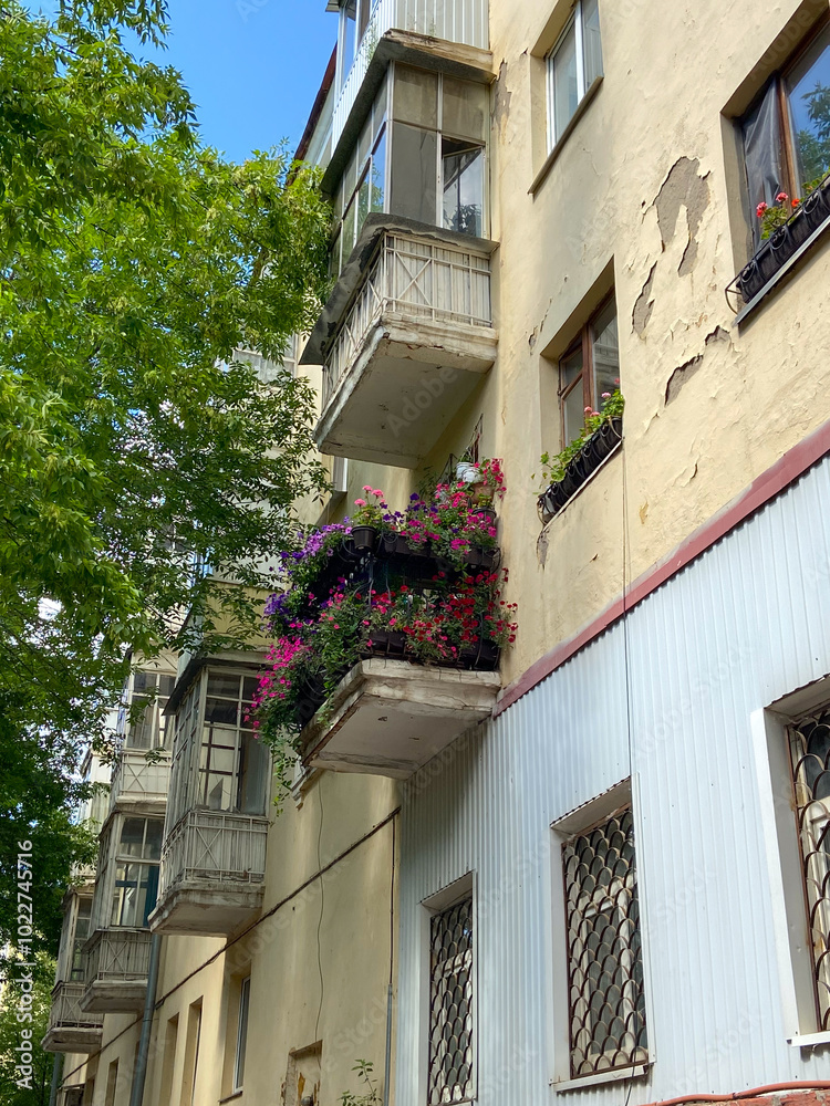 Vibrant urban apartment building stands tall, with colorful flowers adorning its balconies against a backdrop of lush green trees and a bright blue sky. Harmonious blend of nature and city life Vibrant urban apartment building stands tall, with colorful flowers adorning its balconies against a backdrop of lush green trees and a bright blue sky. Harmonious blend of nature and city life