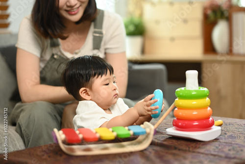 Loving young mother and cute toddler boy playing with educational didactic toy in living room