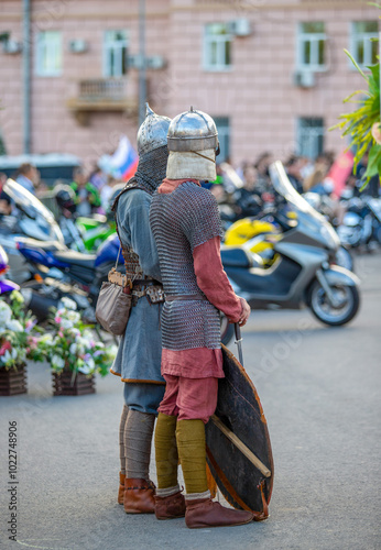 Two men dressed in medieval armor stand on a street next to a motorcycle