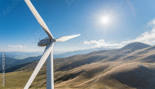 A wind turbine stands tall against a bright sky on a sunny day in a mountainous landscape, showcasing renewable energy in action