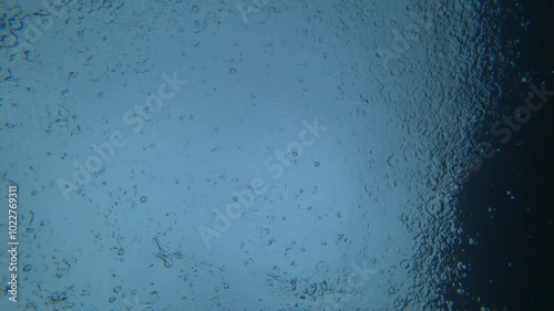 View from under the water to the sky and rain. Drops fall on the surface of the water create water circles. Gray clouds, light from the sky and splashes from drops are visible. An unusual look