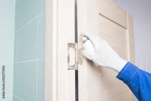 a master in white gloves lubricates a door hinge with oil