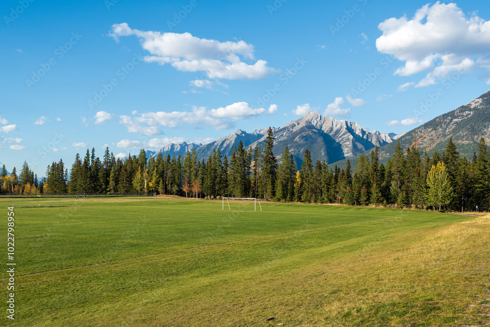 Fototapeta premium Three Sisters Sports Complex Multi-use Field & Playground. Canmore, Alberta, Canada. Canadian Rockies mountain range over the blue sky in the background.