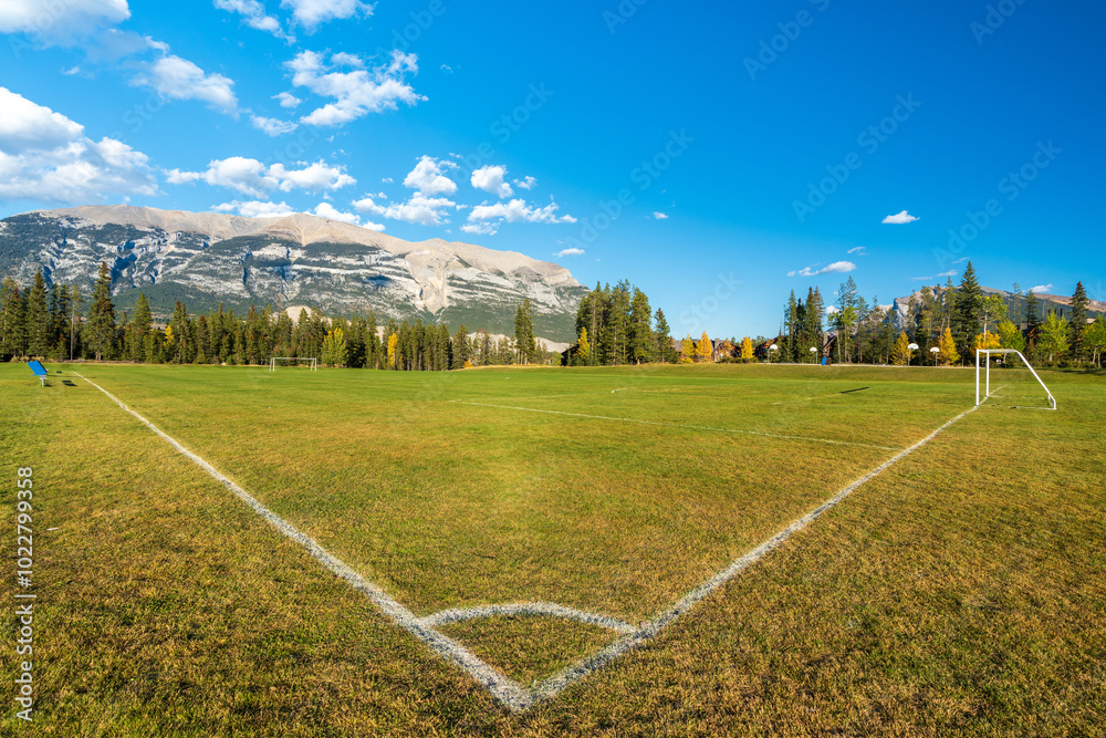 Three Sisters Sports Complex Multi-use Field & Playground. Canmore, Alberta, Canada. Canadian Rockies mountain range over the blue sky in the background. Three Sisters Sports Complex Multi-use Field & Playground. Canmore, Alberta, Canada. Canadian Rockies mountain range over the blue sky in the background.