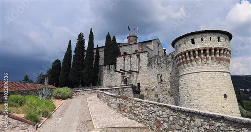 Static video shows the main entrance with an ancient drawbridge to Brescia historic castle with flags of Italy, Brescia, and the EU flying from the central tower photo