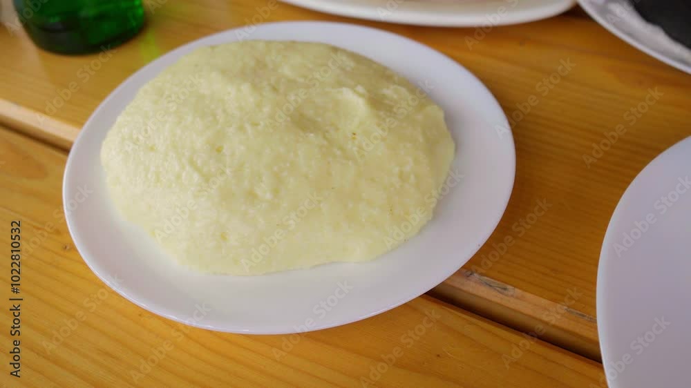 Serving of hominy, traditional dish made of corn flour, takes place at table in restaurant. This hearty dish of Romanian and Georgian cuisine has creamy, delicious taste, perfect for lunch or dinner Serving of hominy, traditional dish made of corn flour, takes place at table in restaurant. This hearty dish of Romanian and Georgian cuisine has creamy, delicious taste, perfect for lunch or dinner