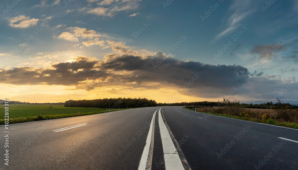 Winding road under a dramatic sky during sunset in a rural landscape with fields and trees Winding road under a dramatic sky during sunset in a rural landscape with fields and trees