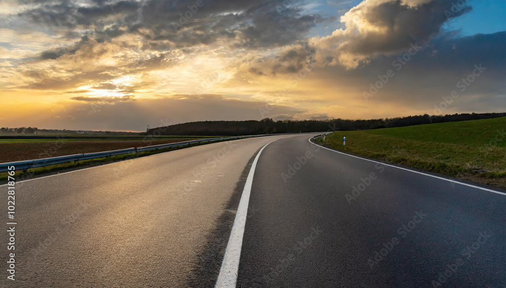 Naklejka premium Scenic winding road under a dramatic sky at sunset in the countryside