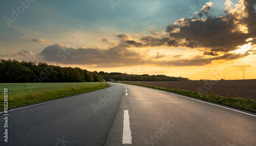 A winding road through fields under a dramatic sunset sky with colorful clouds in the background