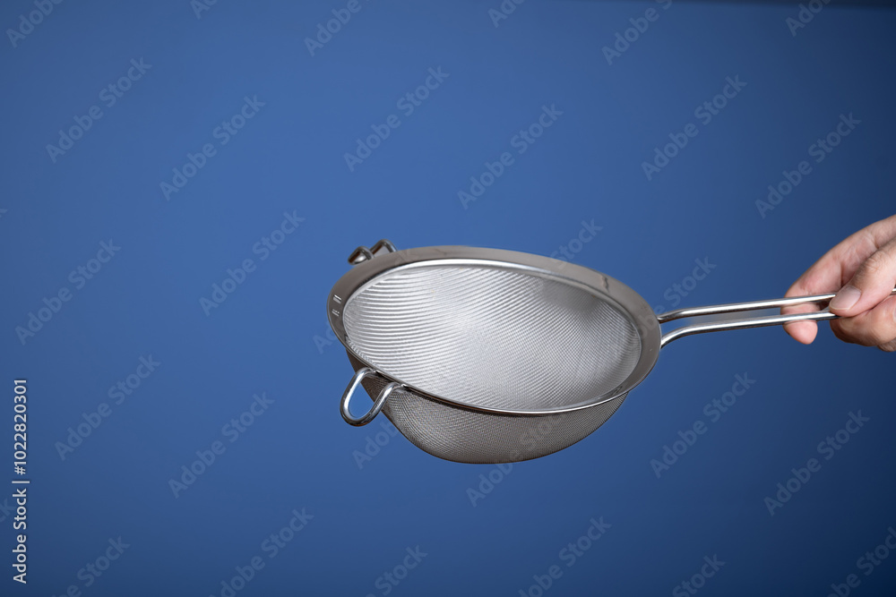 Stainless steel sieve. Held by hand by Caucasian male hand. Close up studio shot, isolated on blue Stainless steel sieve. Held by hand by Caucasian male hand. Close up studio shot, isolated on blue