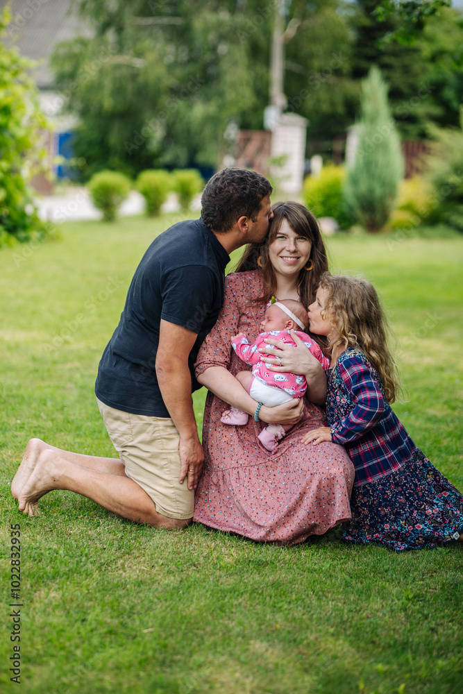 Joyful family kneels in the green grass as the mother cradles their newborn baby Joyful family kneels in the green grass as the mother cradles their newborn baby