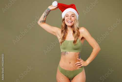 Young lady woman with slim skinny body perfect skin wears top bra lingerie red Santa Claus hat stand wink isolated on plain pastel green background. Lifestyle diet fit, New Year celebration concept. photo