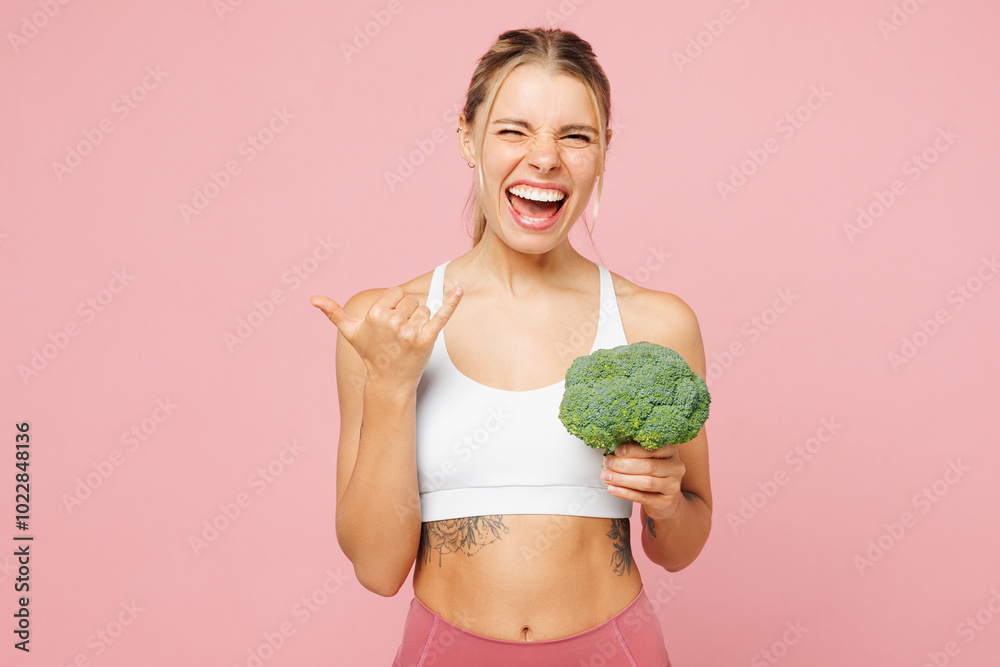 Young excited woman wear white top casual clothes hold in hand broccoli do winner gesture isolated on plain pastel light pink background. Proper nutrition healthy fast food unhealthy choice concept. Young excited woman wear white top casual clothes hold in hand broccoli do winner gesture isolated on plain pastel light pink background. Proper nutrition healthy fast food unhealthy choice concept.