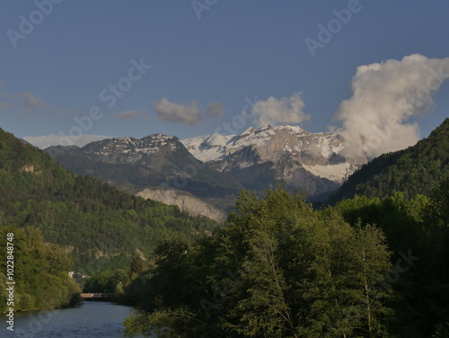 arve river surrounded by trees, in sunset light in cluses, haute savoie, and alps mountains in the background. Panoramic landscape in springtime photo